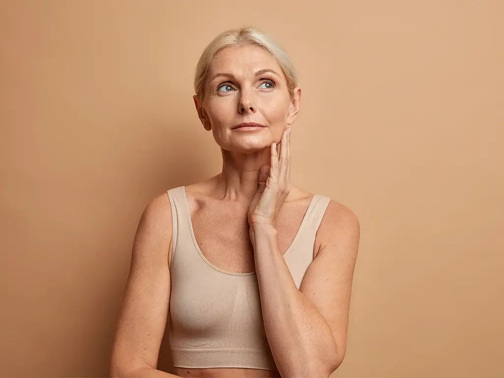 Older woman touching her face, representing healthy aging and skin longevity